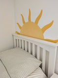 Load image into Gallery viewer, White crib with a yellow sun-shaped headboard on a light-colored wall.