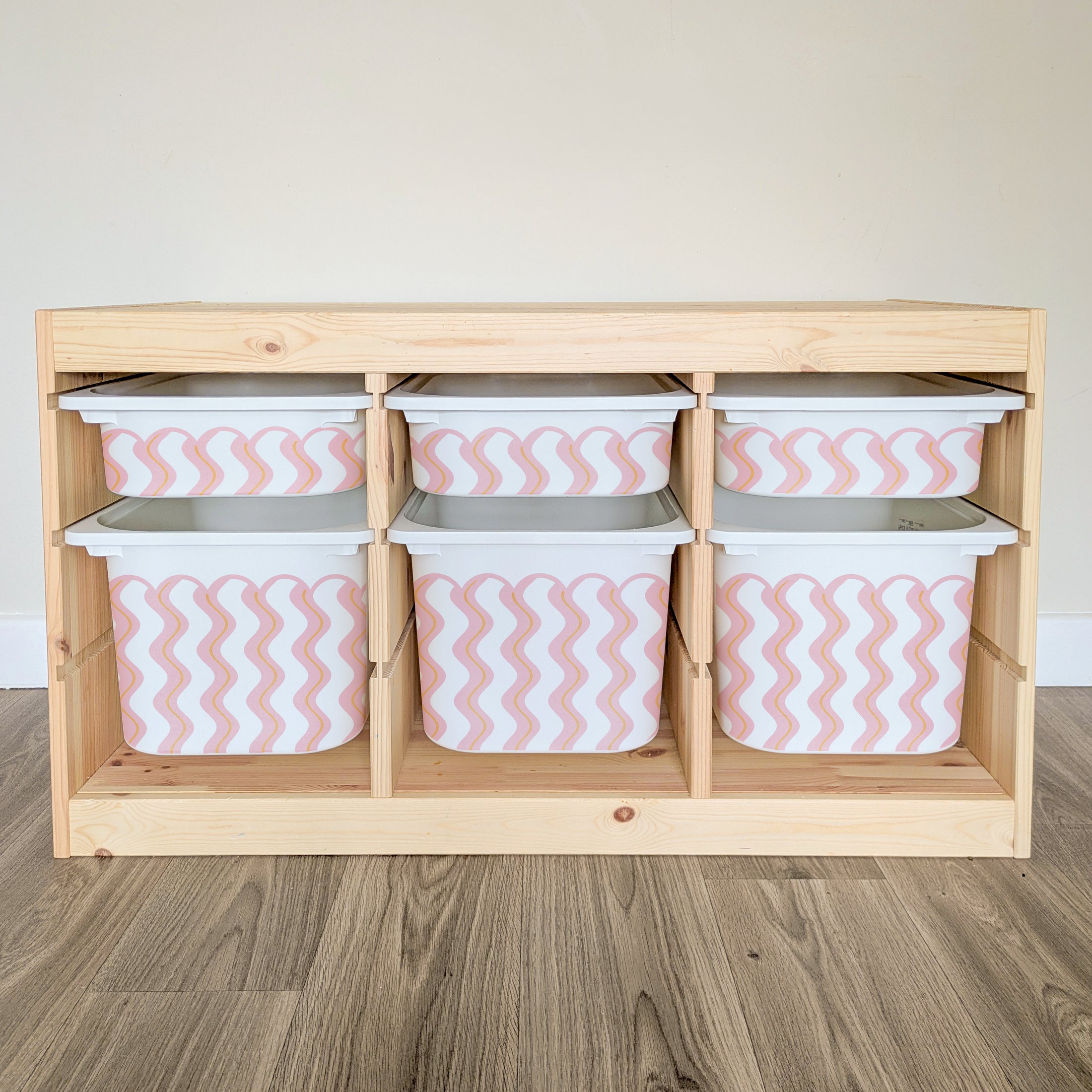 A wooden shelf with six compartments, each containing a white plastic bin with a pink and white striped pattern.