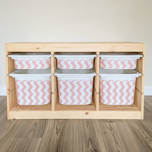 A wooden shelf with six compartments, each containing a white plastic bin with a pink and white striped pattern.