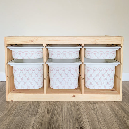 A wooden shelf with six white storage bins arranged in two rows of three, each bin featuring a pink and white patterned design.