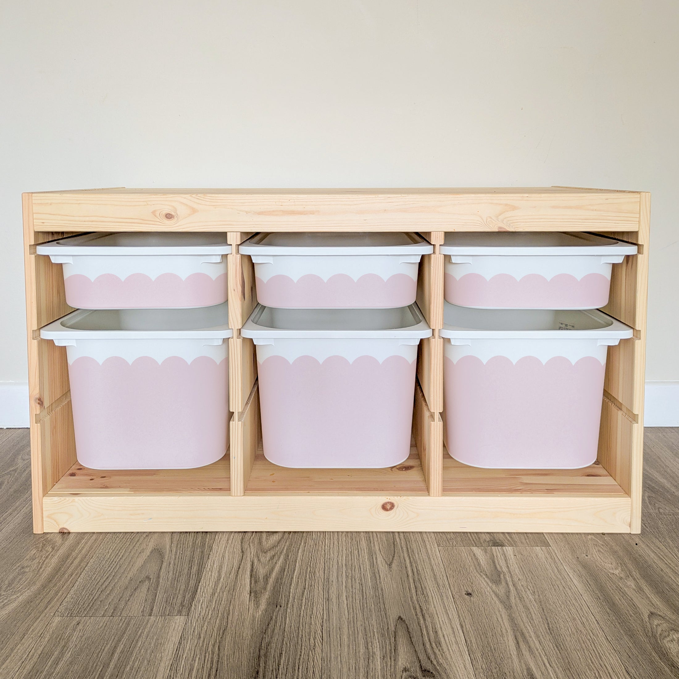 A wooden storage unit with six pink and white storage bins arranged in two rows of three.