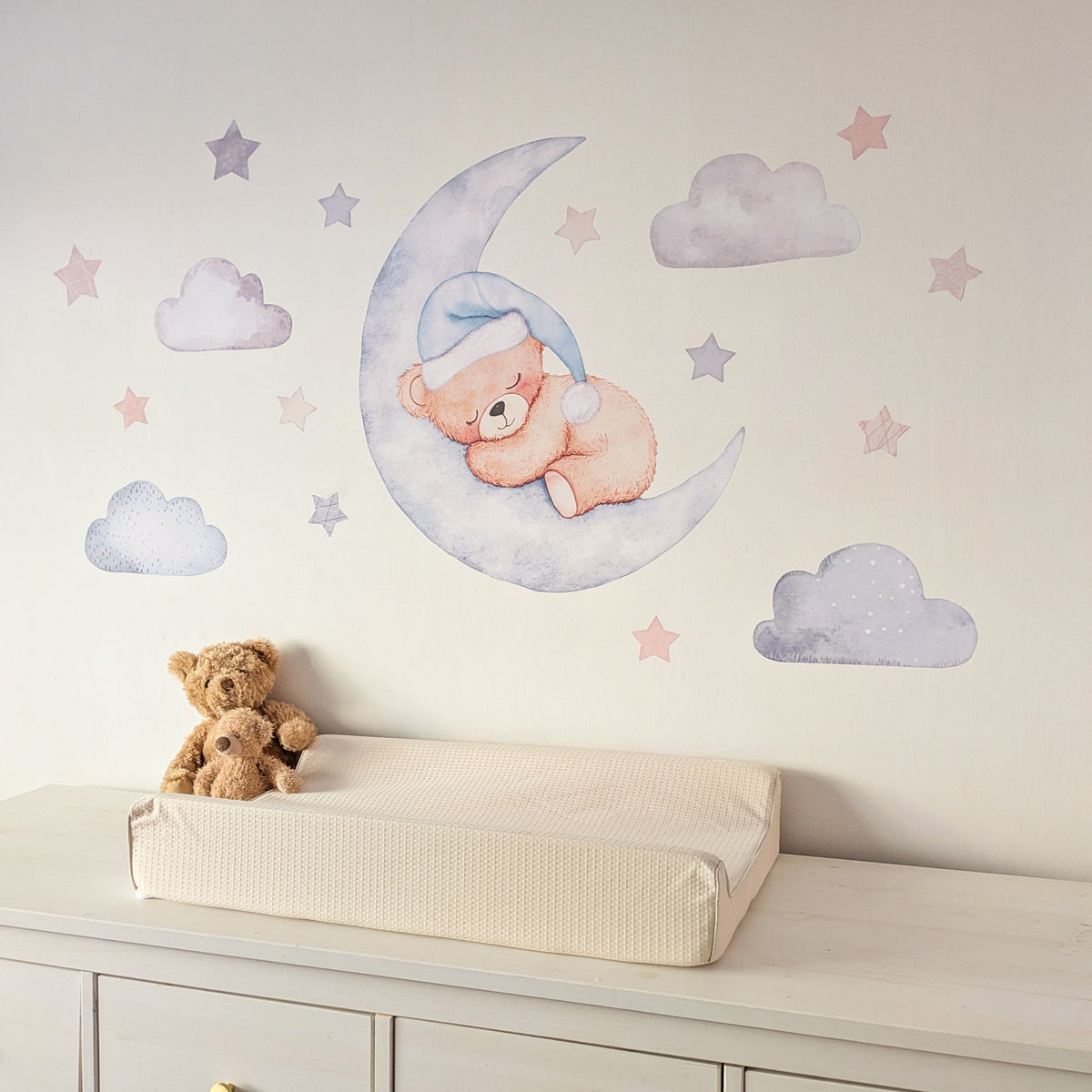 Blue teddy bear sleeping on a crescent moon with clouds and stars on a nursery wall