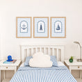 Load image into Gallery viewer, Coastal nursery prints above a bed with blue striped bedding
