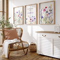 Load image into Gallery viewer, a room with a chair, table, and three paintings on the wall
