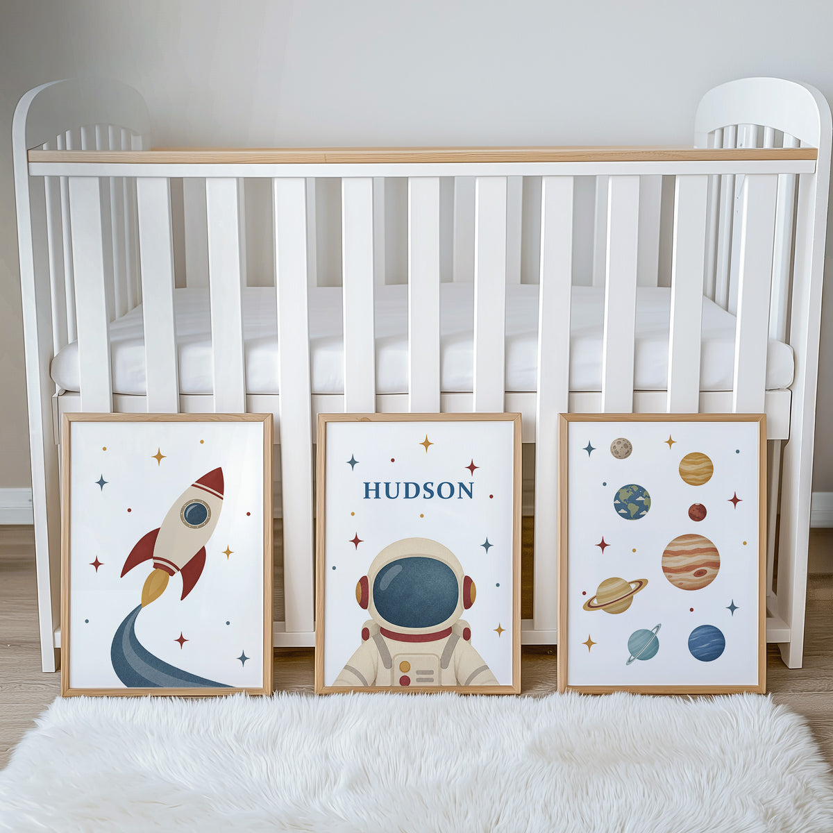 Set of three prints showing rocket, personalised astronaut and planets, beside cot display