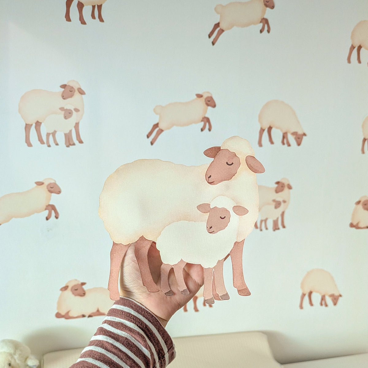 Close-up of a sheep and lamb fabric wall sticker held against a nursery wall
